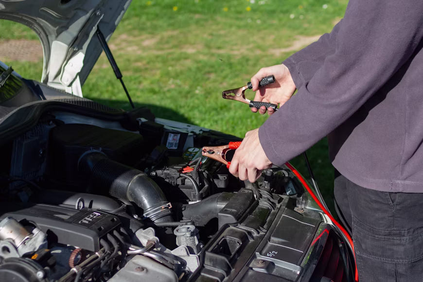 Mechanic working under the hood of a car using jumper cables